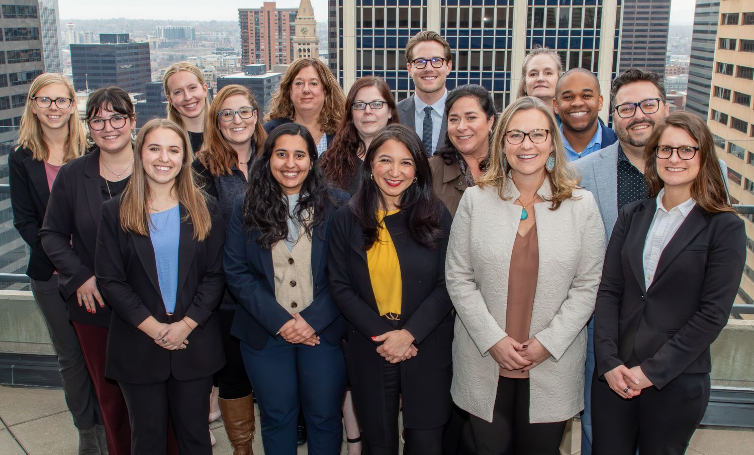 Large group of professionals posing together on rooftop with city skyline in background.