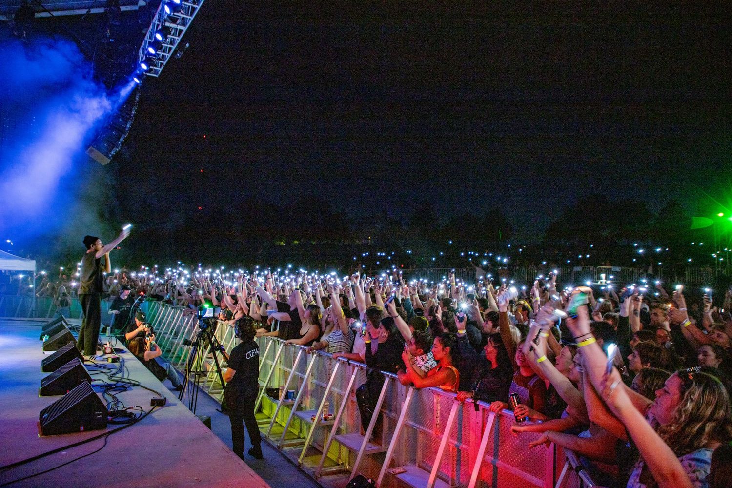 Performer on stage energizes massive crowd with phone lights raised at outdoor University of Denver concert.