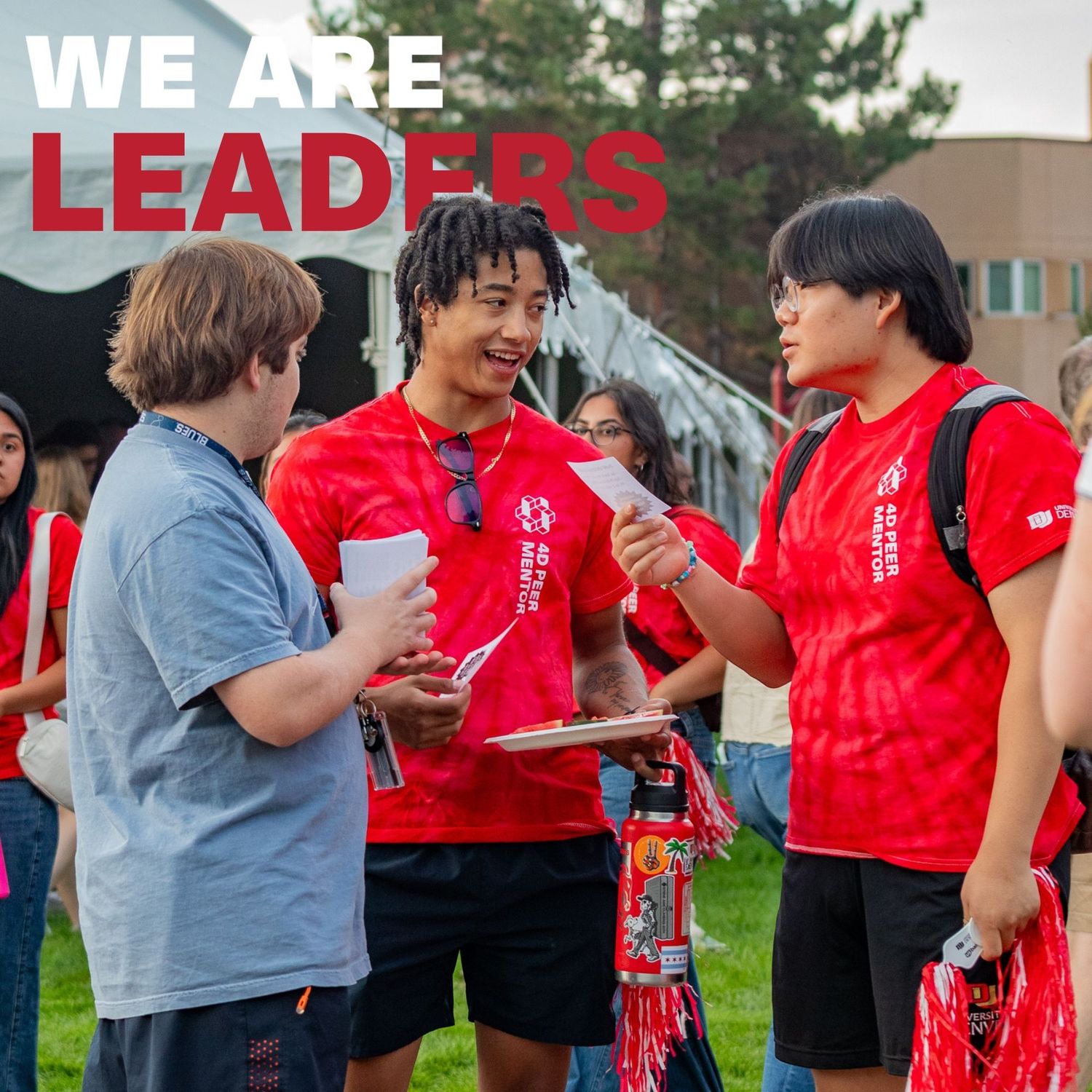 Students in red shirts engage in conversation outdoors at a campus event with text reading We Are Leaders.