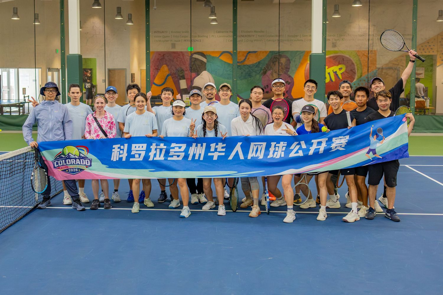 Group photo of participants at the Colorado Chinese Tennis Open tournament, posing together on an indoor tennis court with a banner.