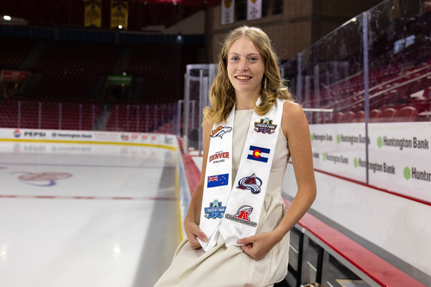 Young woman in white dress with sports team sash poses at an ice hockey rink arena.