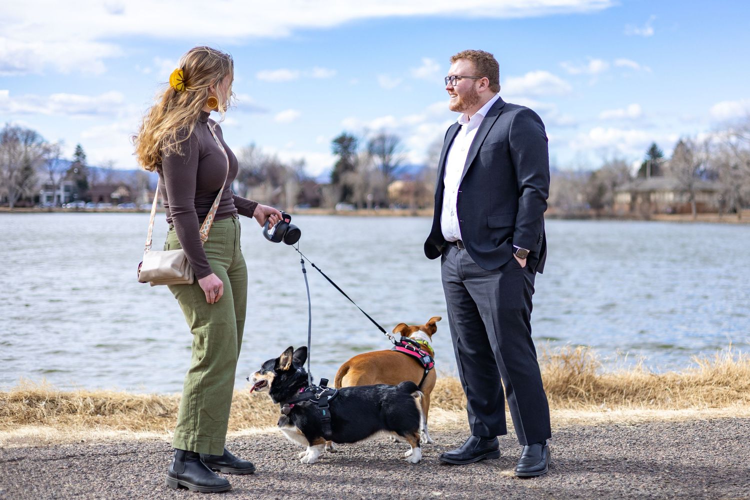 A couple takes photos along a waterfront path with their dog on a sunny autumn day.