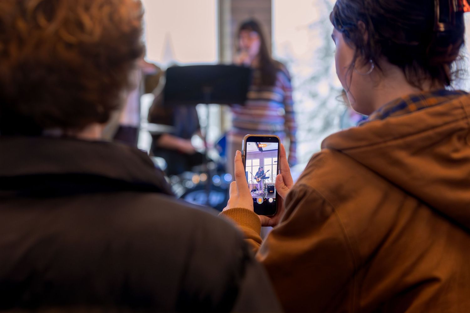 Person recording a live music performance on a smartphone at an indoor event.
