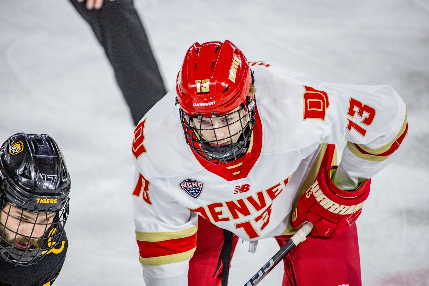 Denver Pioneers hockey player #13 in white jersey and red helmet faces off during an NCAA college hockey game.