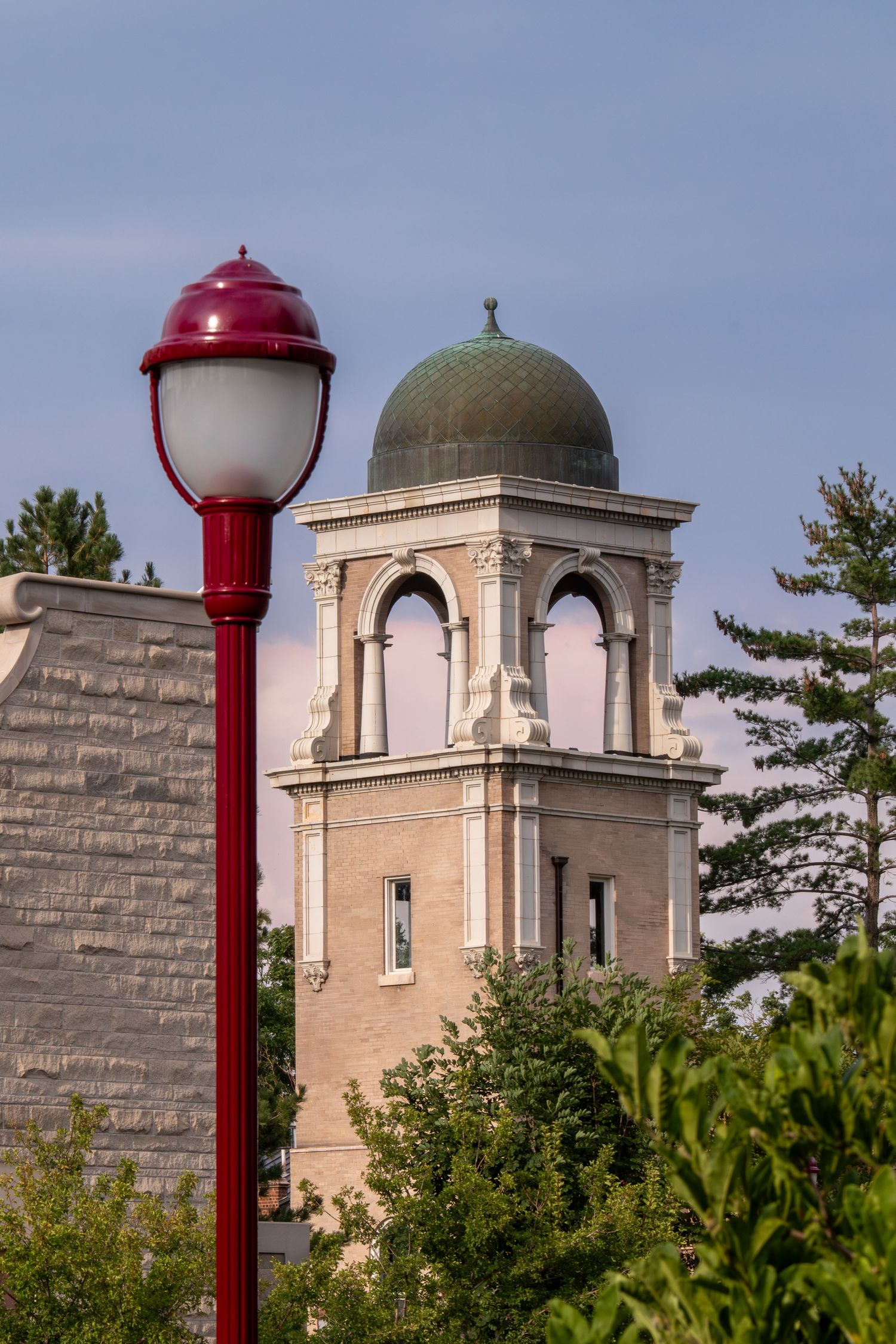 Historic campus bell tower with green copper dome beside a red street lamp against a blue sky.