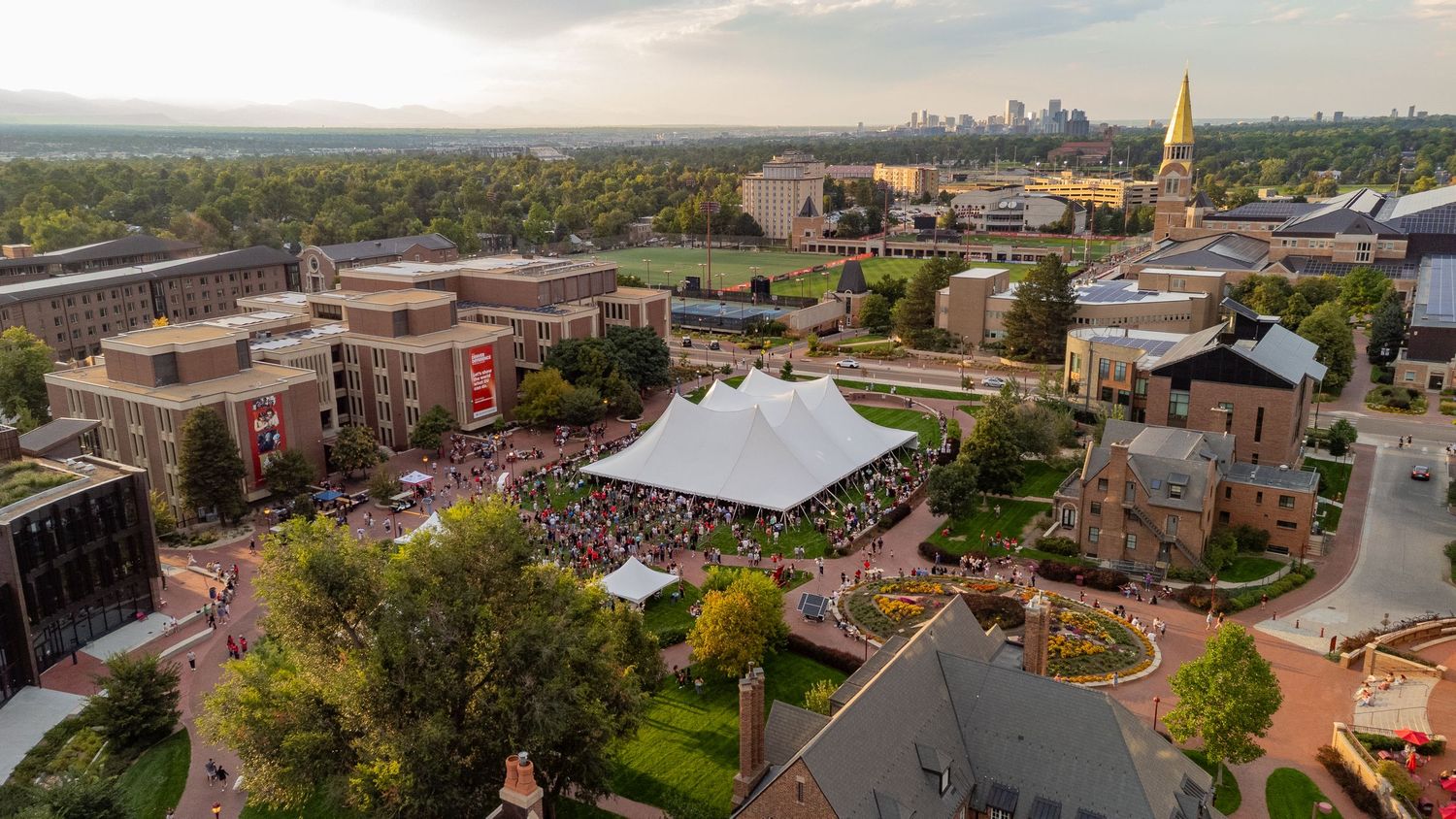 Panoramic aerial view of a college campus with brick buildings, green spaces, and modern architecture under cloudy skies.