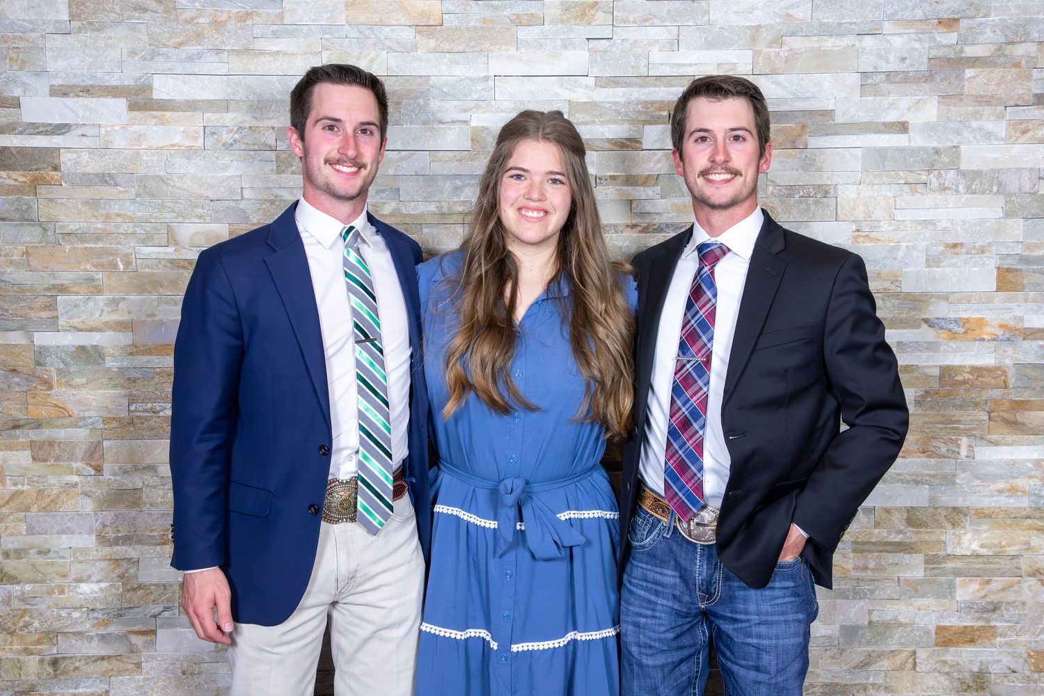 Three people in business attire pose together against a textured stone wall background.