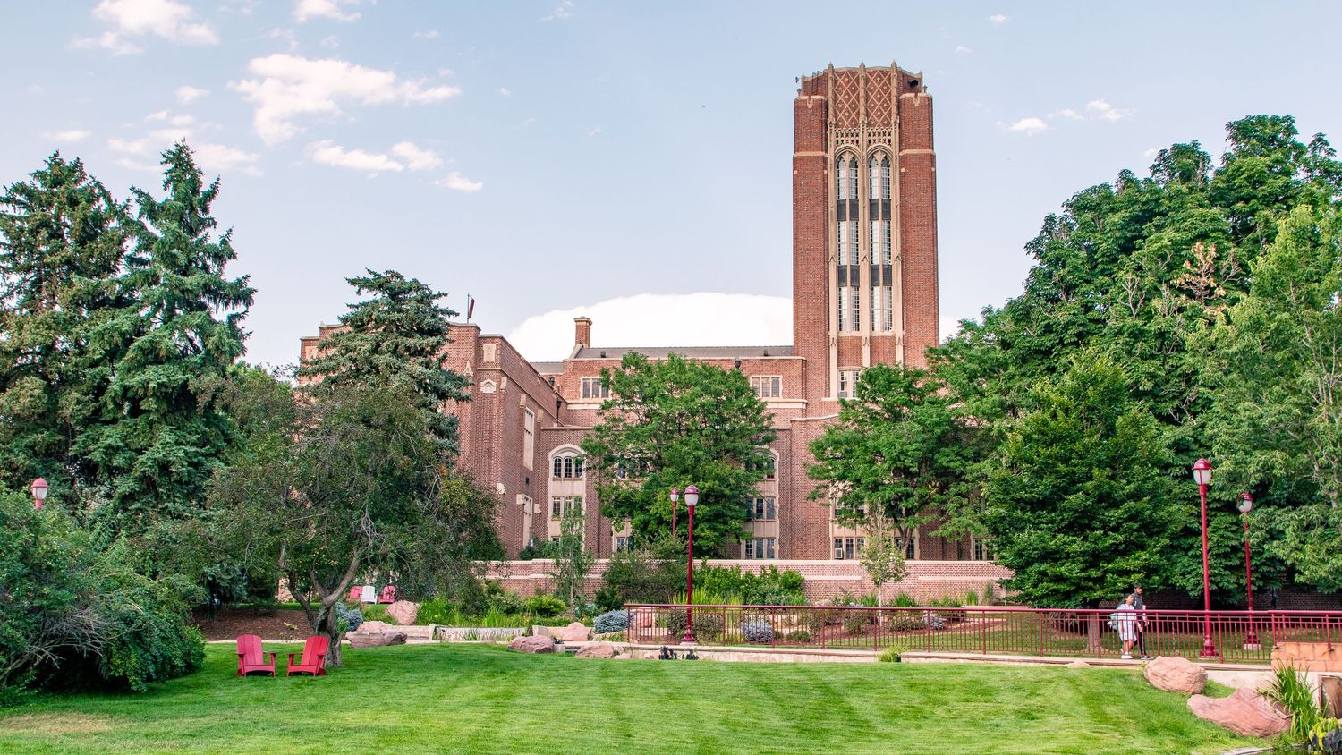 A panoramic view of a university campus with brick buildings, clock tower, and lush green trees under blue skies.