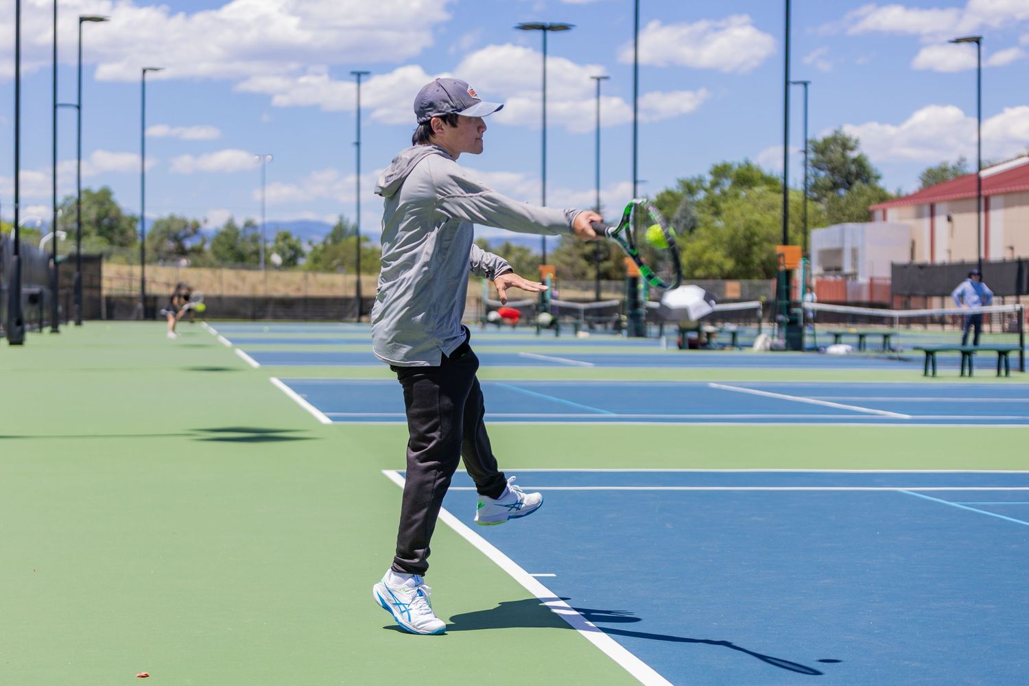 Person playing pickleball on an outdoor blue court on a sunny day, mid-swing with a paddle.