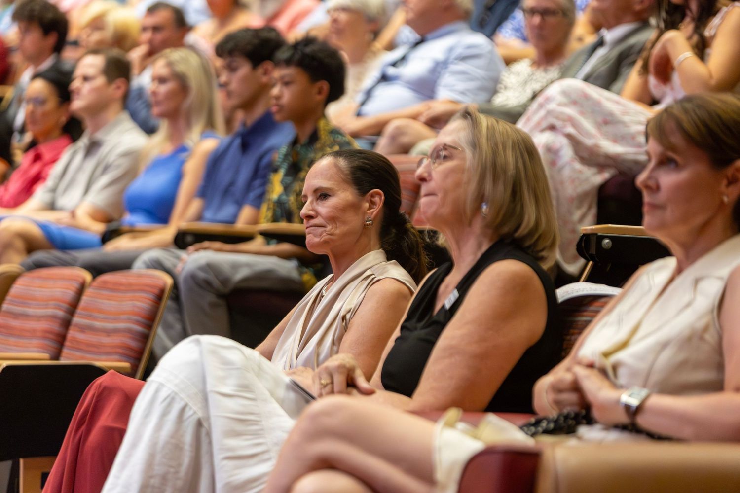 Audience members seated in red chairs at an indoor conference or seminar event, listening attentively to a presentation.