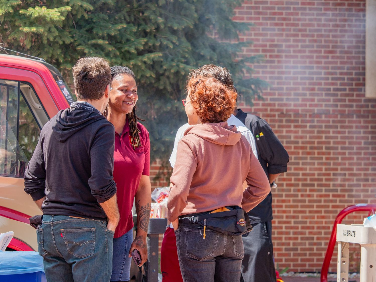 Three people socializing outdoors near a brick building at a casual daytime gathering event.