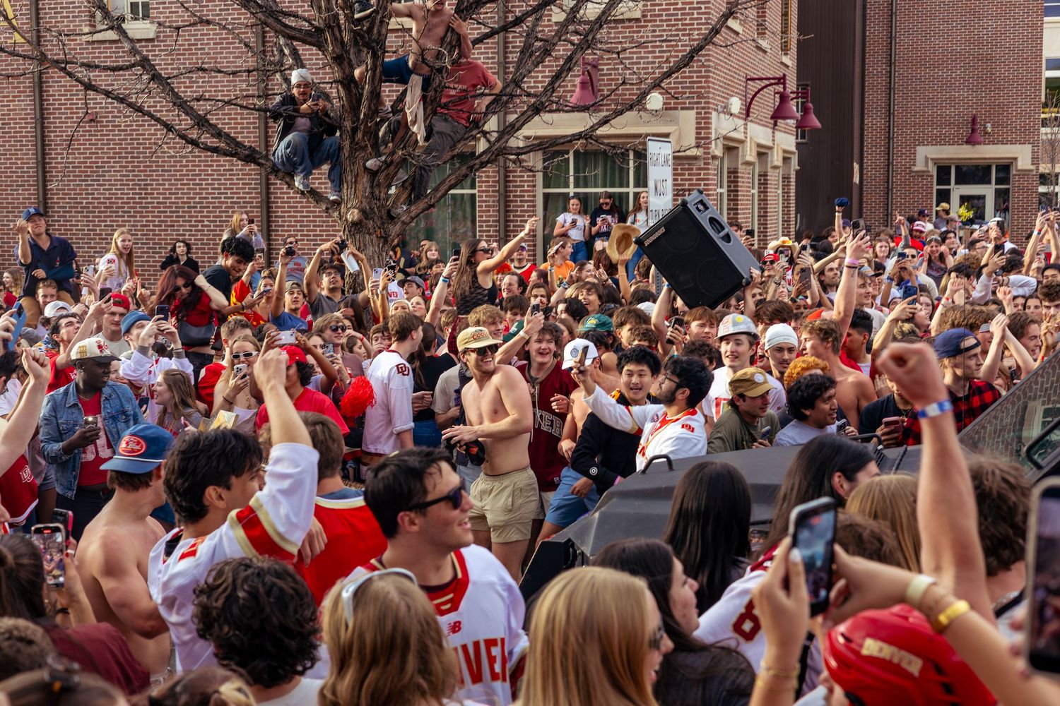 Large crowd of sports fans celebrating outdoors, raising fists, wearing red and white jerseys at a lively street rally.