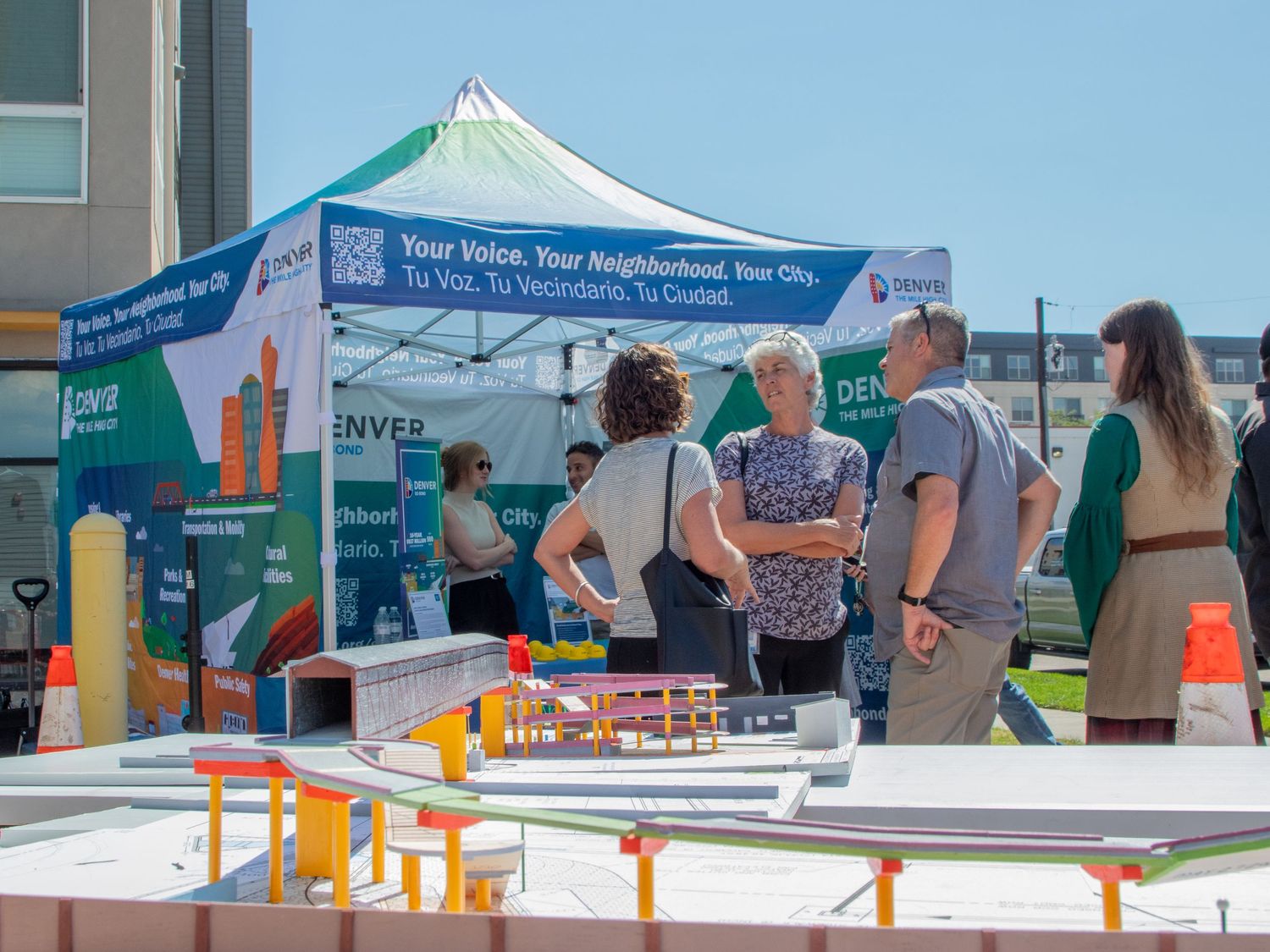 Outdoor community event with multiple white tents and vendor booths set up in a parking lot on a sunny day.