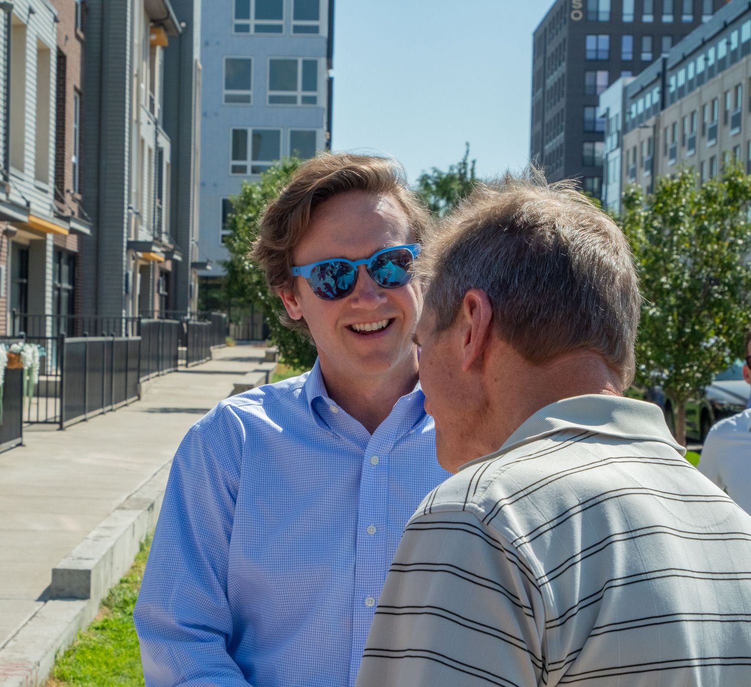 Two people in casual attire sit and chat together on outdoor steps of a modern building on a sunny day.