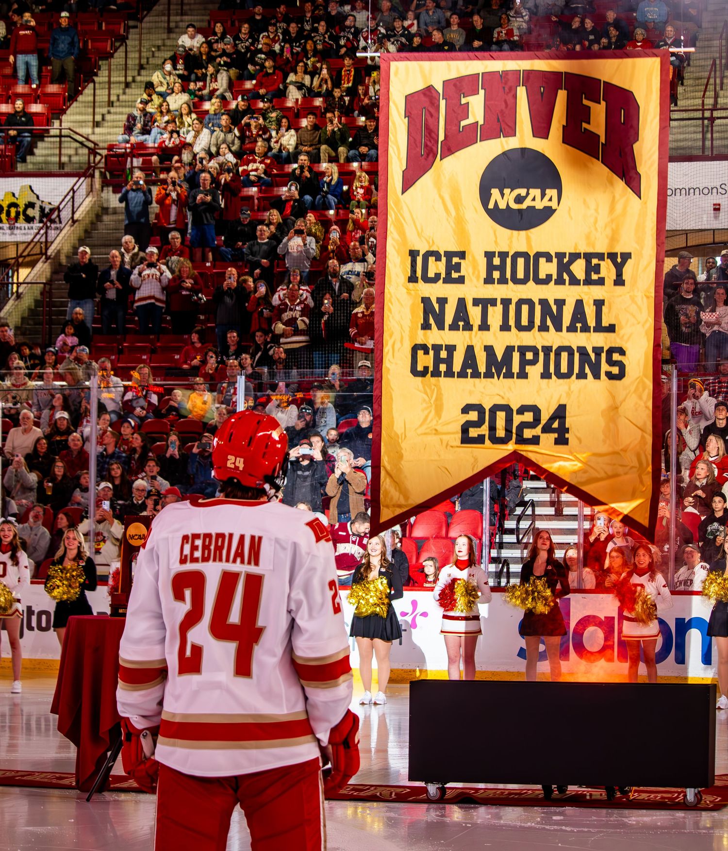 Denver Pioneers hockey player watches 2024 NCAA Ice Hockey National Champions banner raise at packed arena.