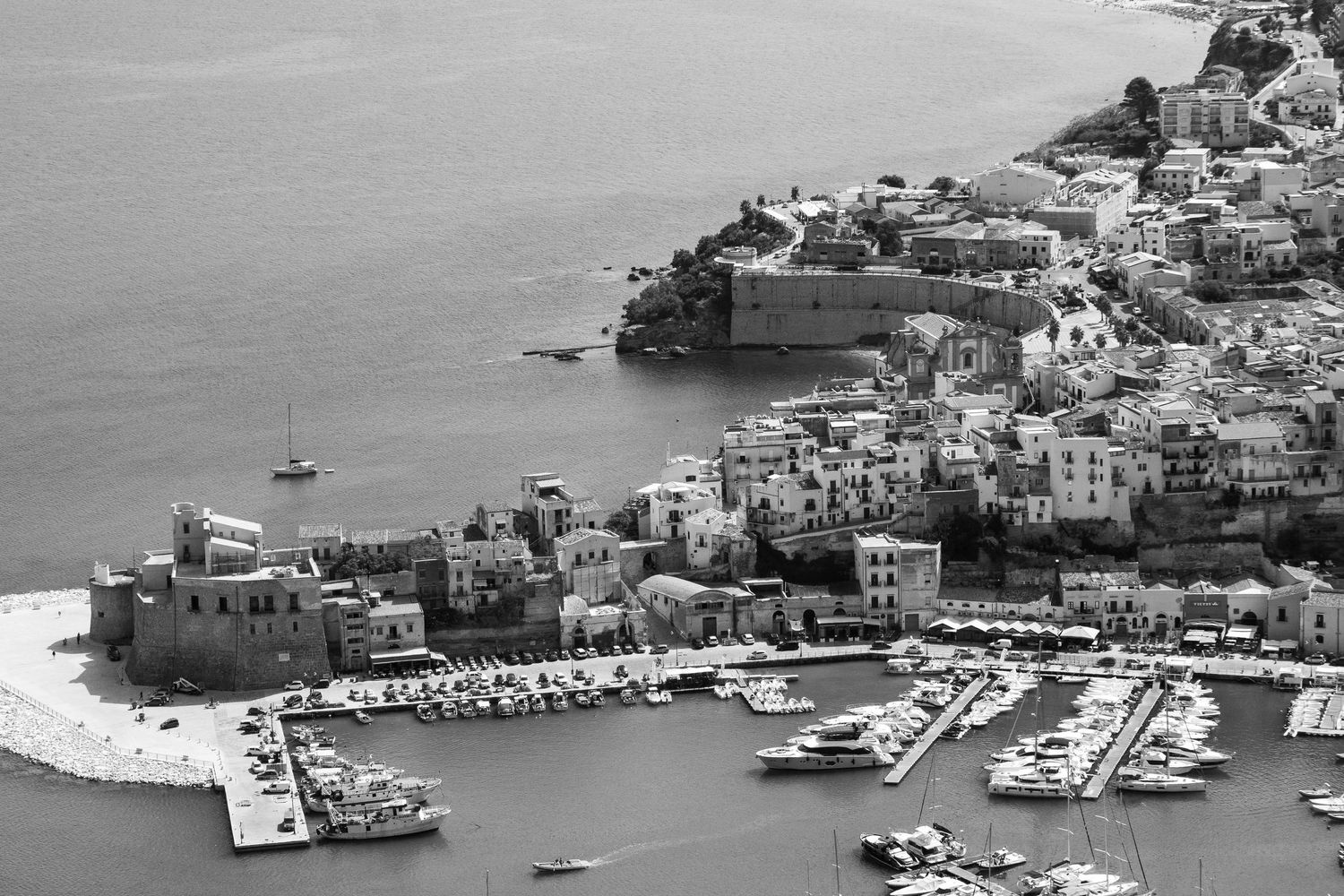 Black and white panoramic view of a Mediterranean coastal town with white buildings cascading down hillsides to a harbor.