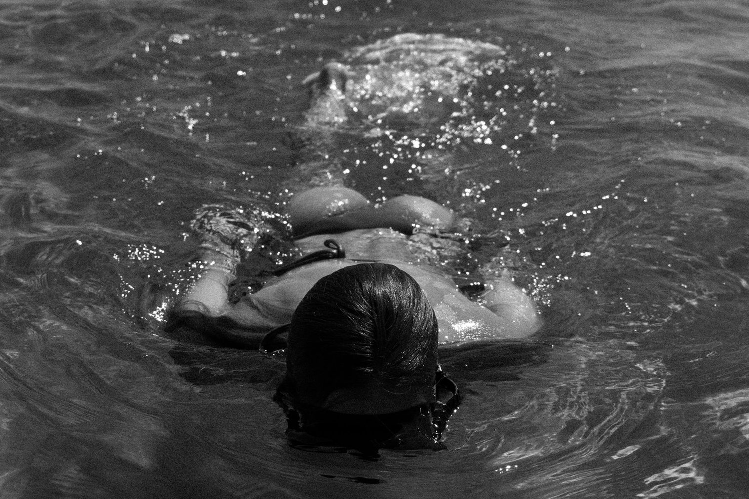 A swimmer splashes through dark water creating ripples and spray in a black and white photograph.