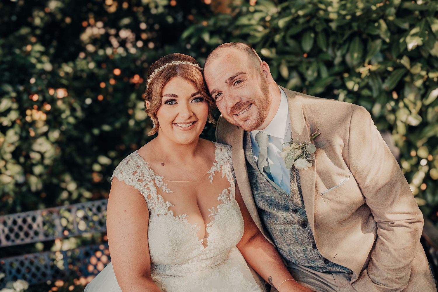 Wedding couple poses in garden setting with natural lighting and foliage backdrop.