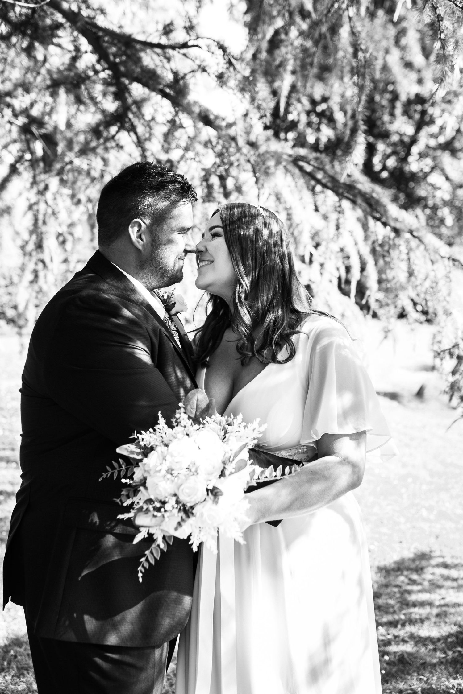 Black and white wedding portrait of couple sharing intimate moment under willow trees.