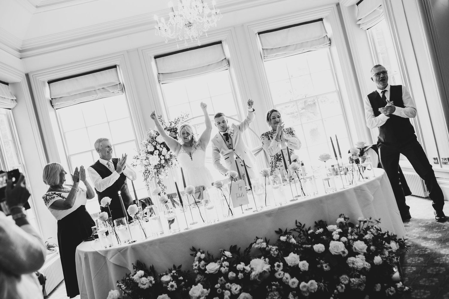 A couple shares their first dance at an elegant wedding reception in a bright ballroom with chandeliers and floral decor.