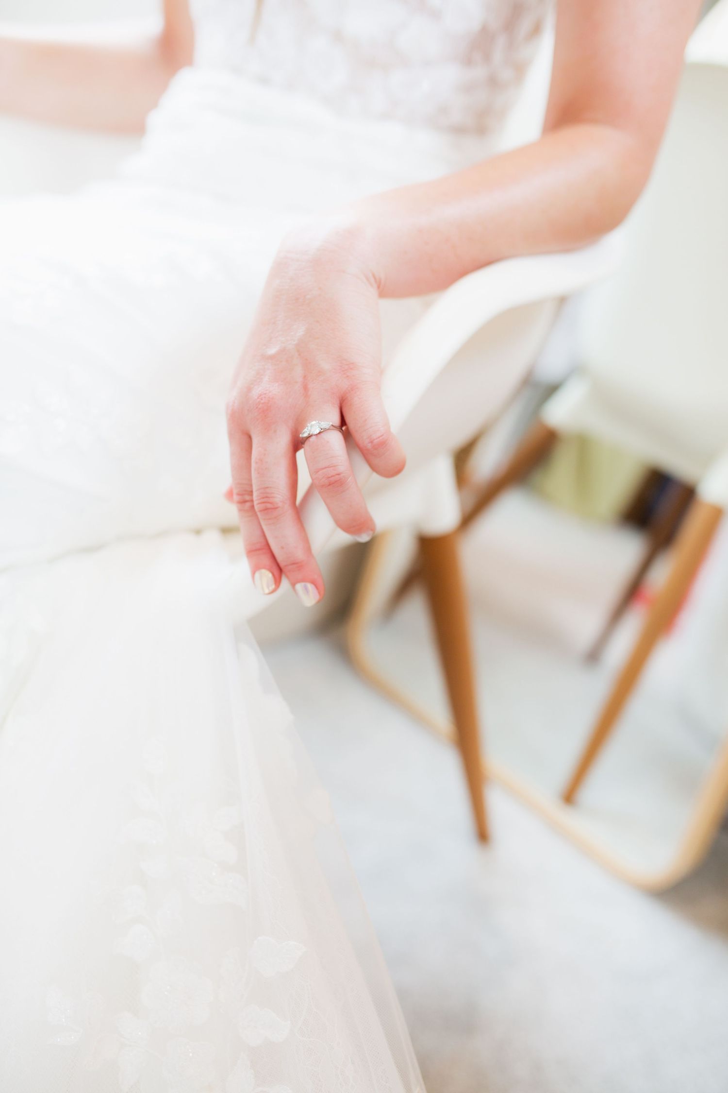 Close-up of a bride's hand showing off her engagement ring against the white fabric of her dress.