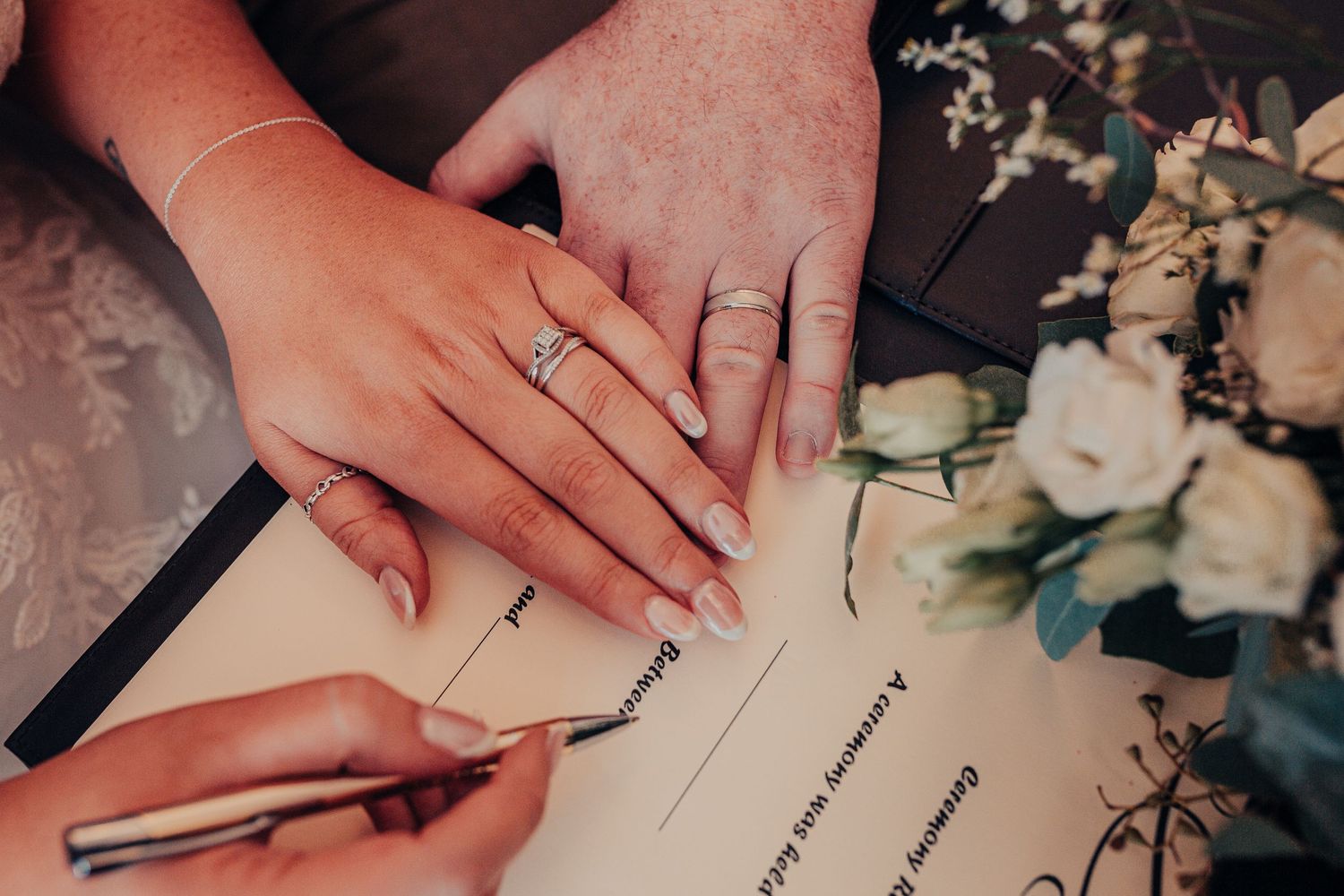 Close-up shots of hands signing wedding documents with rings and floral arrangements visible.