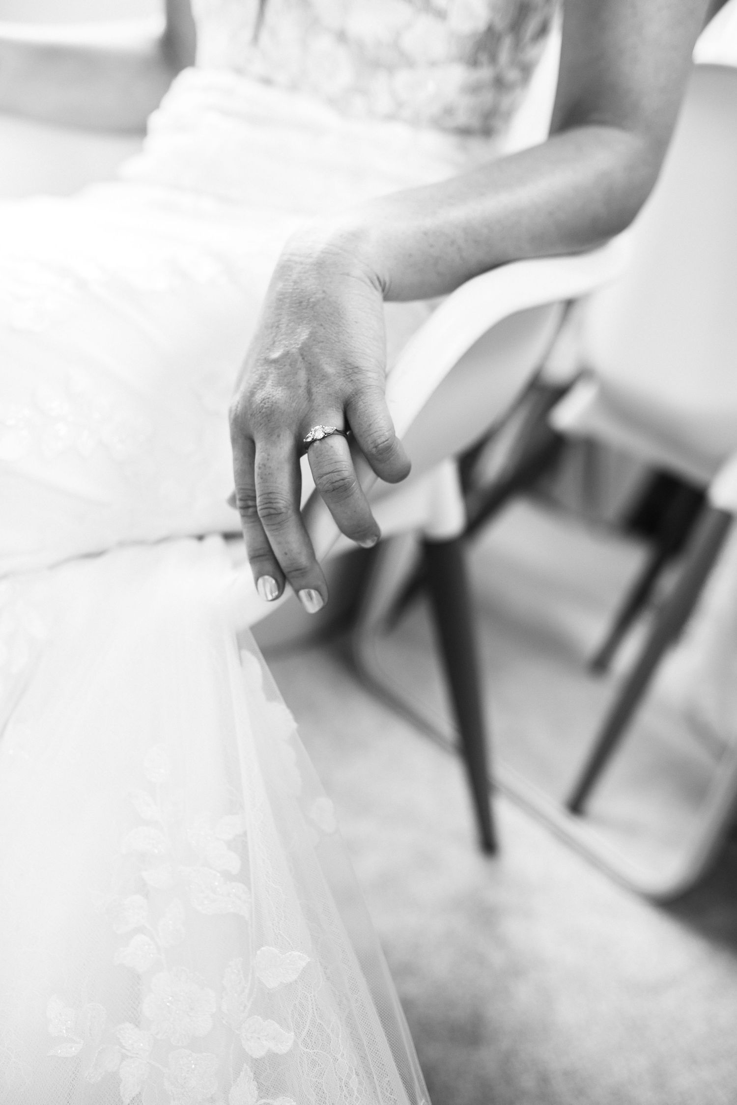 Close-up black and white shot of bride's hand showing engagement ring and lace dress detail.