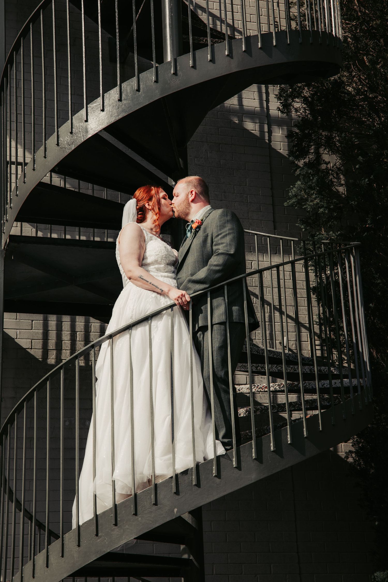 Couple embraces on spiral staircase during romantic wedding photo session.