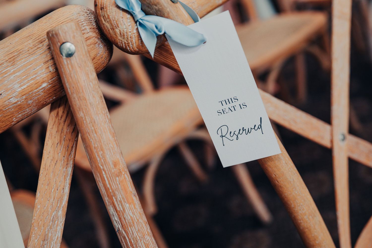 A romantic 'Reserved' tag hanging on a wooden chair at a wedding venue.