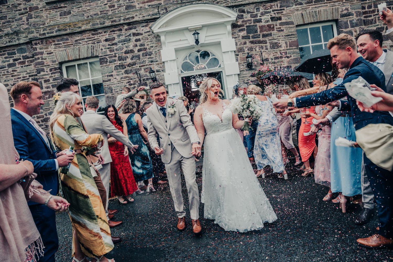 Wedding celebration with guests throwing confetti outside a stone building.