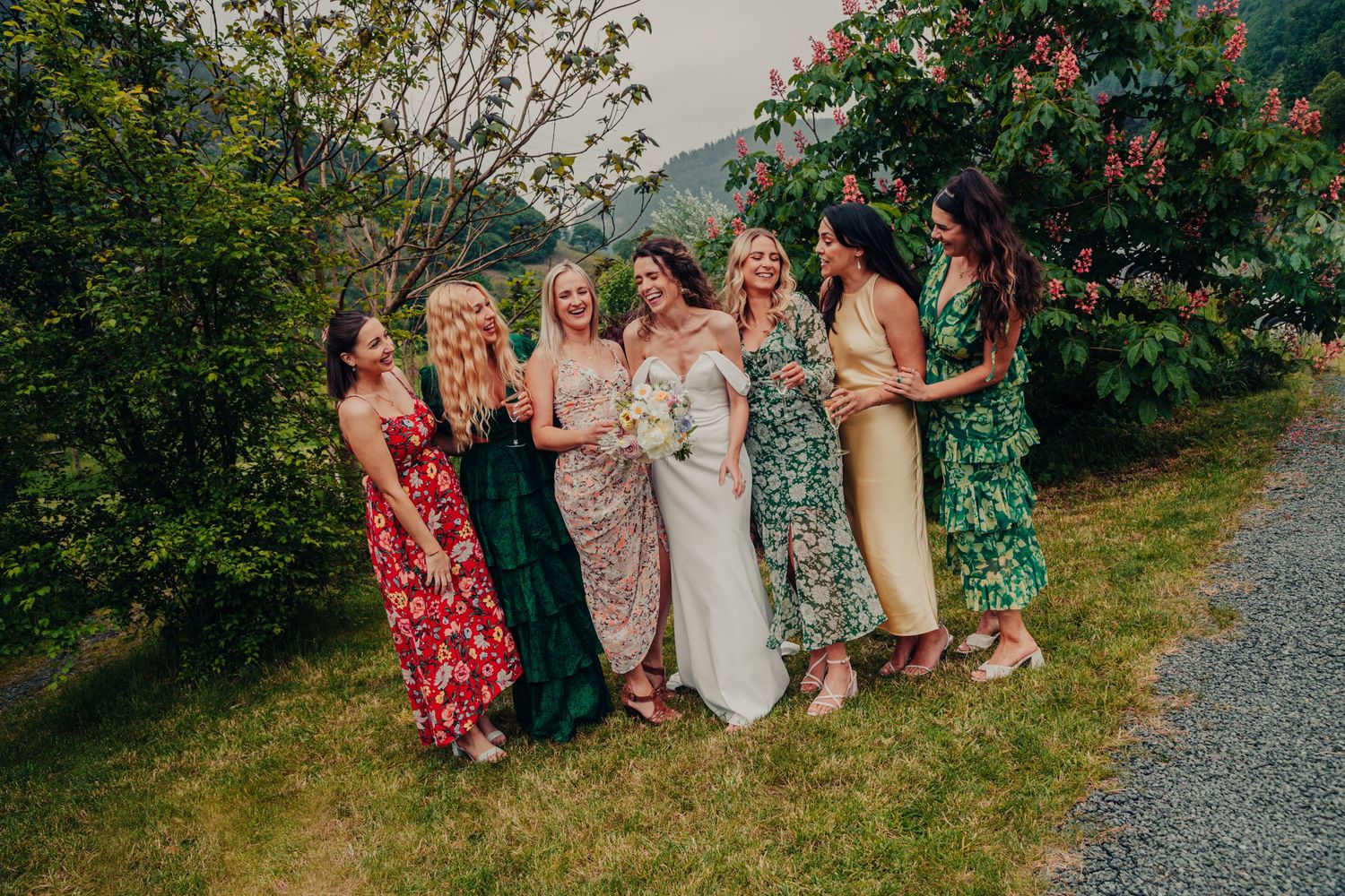 A group in colorful floral dresses and formal attire gather together on a grassy hill during a summer celebration.