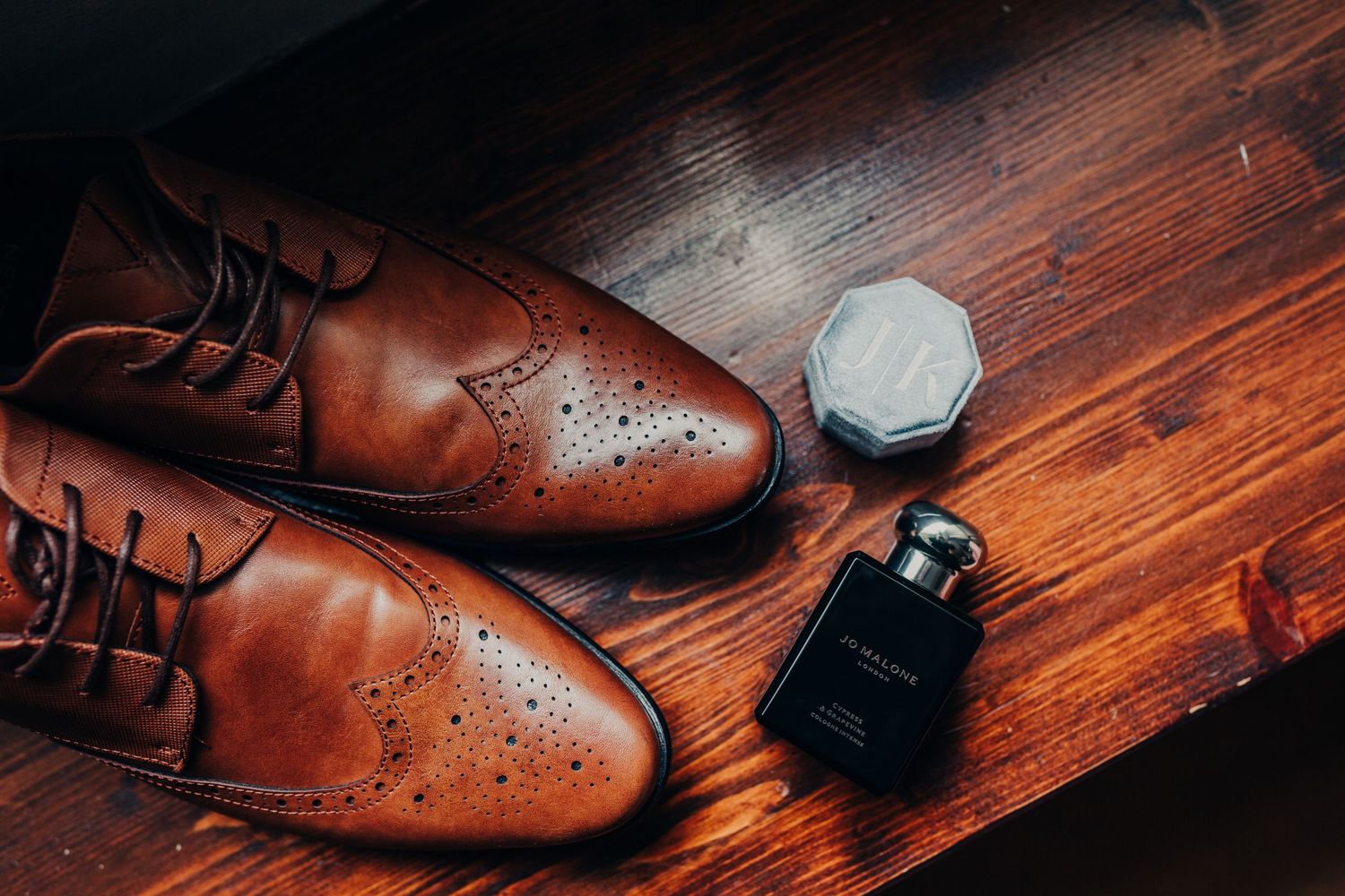 Brown leather dress shoes and cologne bottle on wooden surface.