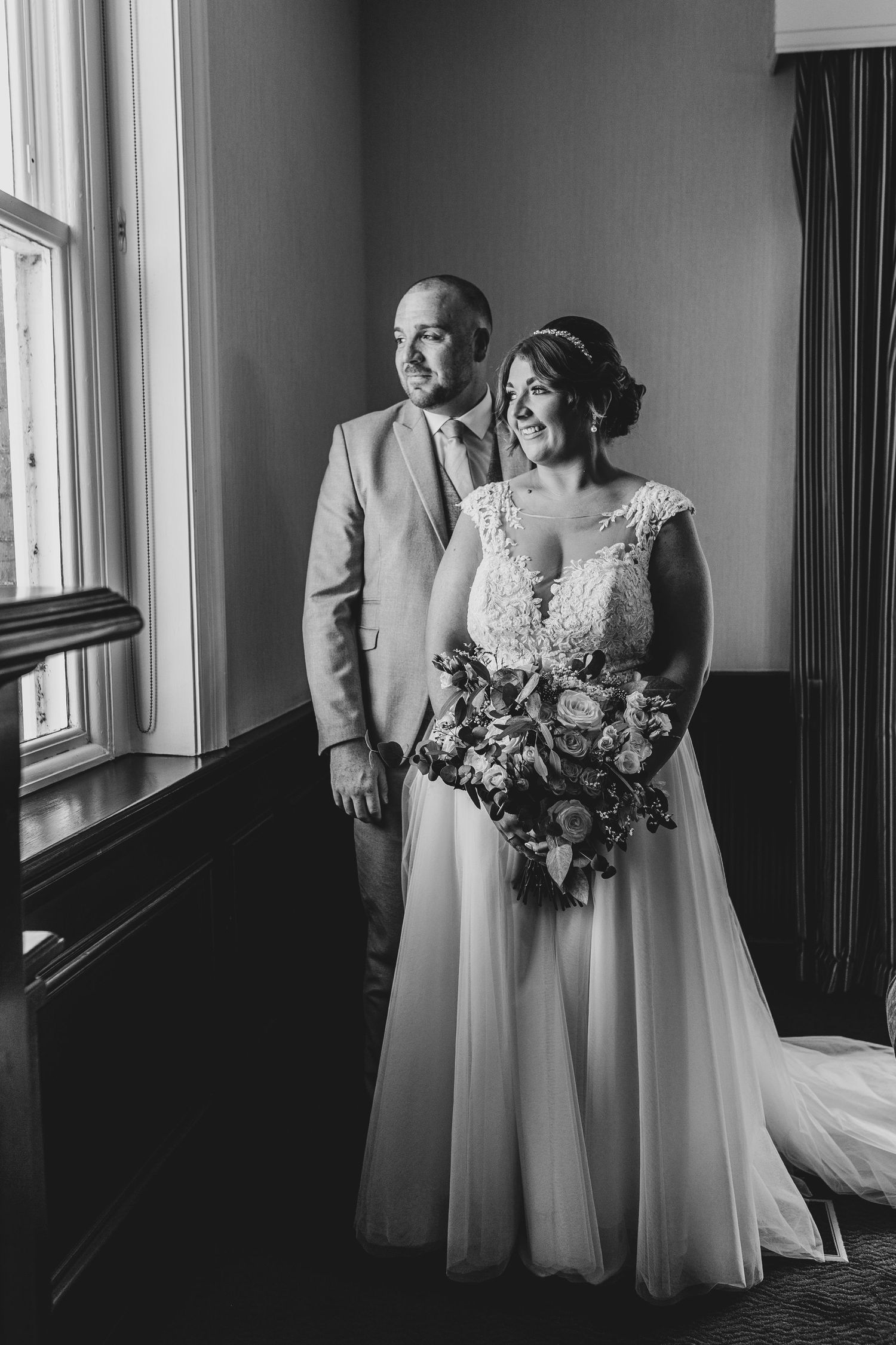 Dramatic black and white wedding portraits taken near large windows in an elegant interior.