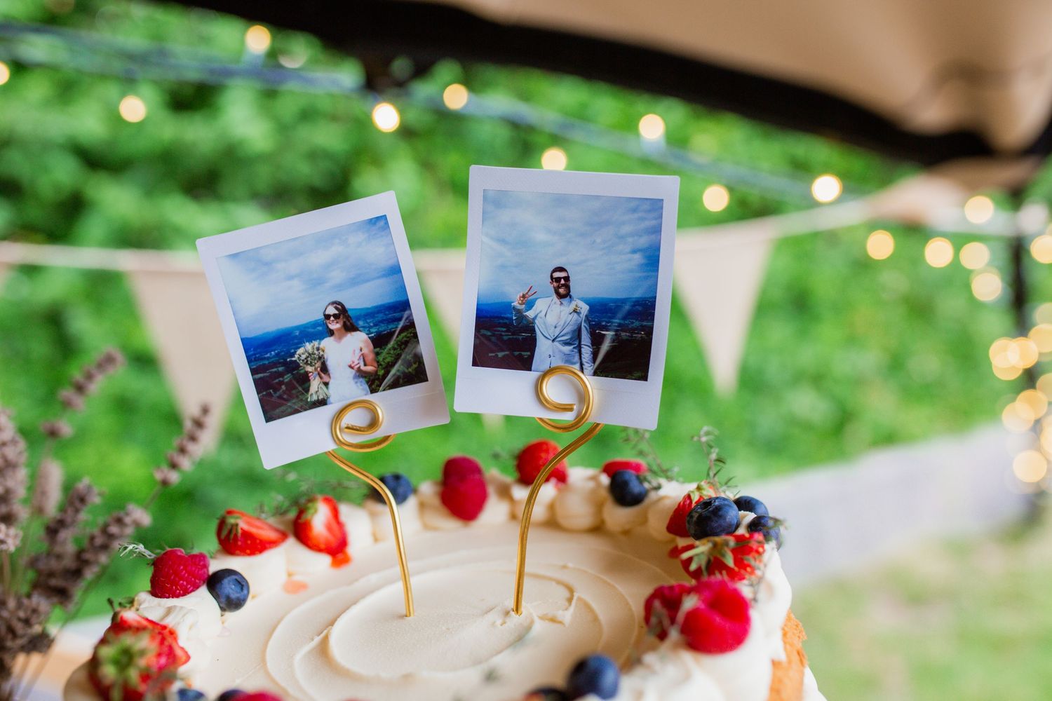 Wedding cake decorated with Polaroid photos, fresh berries, and rustic decor on a wooden surface.