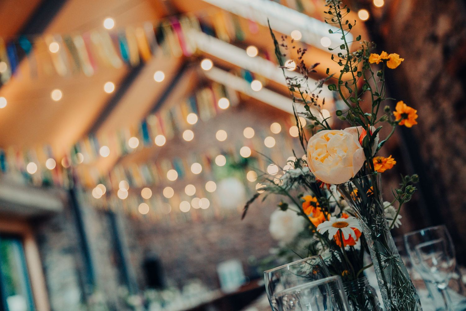 A floral centerpiece with orange flowers and white roses against a blurred background of twinkling lights at dusk.