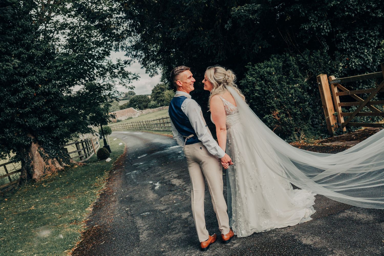 Romantic wedding portraits taken on a tree-lined path with flowing veil details.