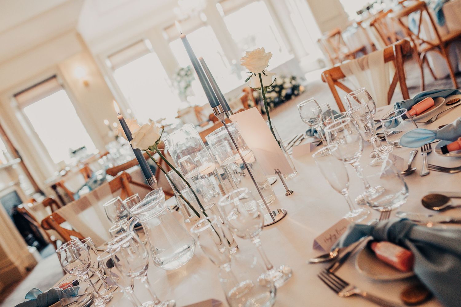 Elegant wedding table setting with tall candles and crystal glassware in natural light.