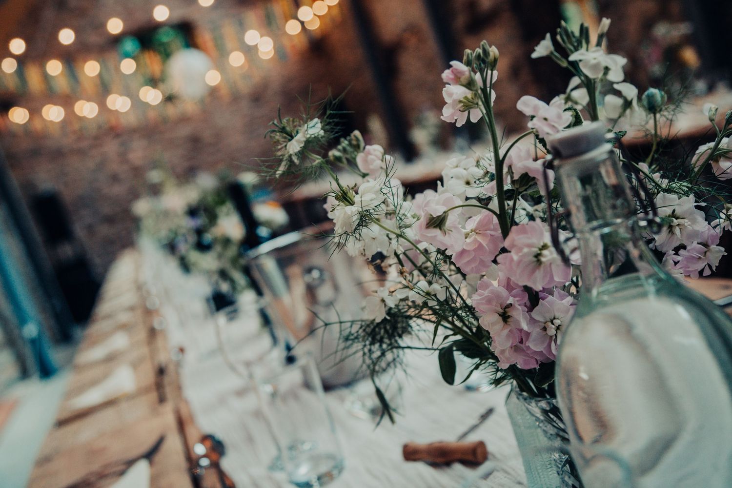 Elegant floral table centerpiece with pink and white blooms at a wedding reception with bokeh lights in background.