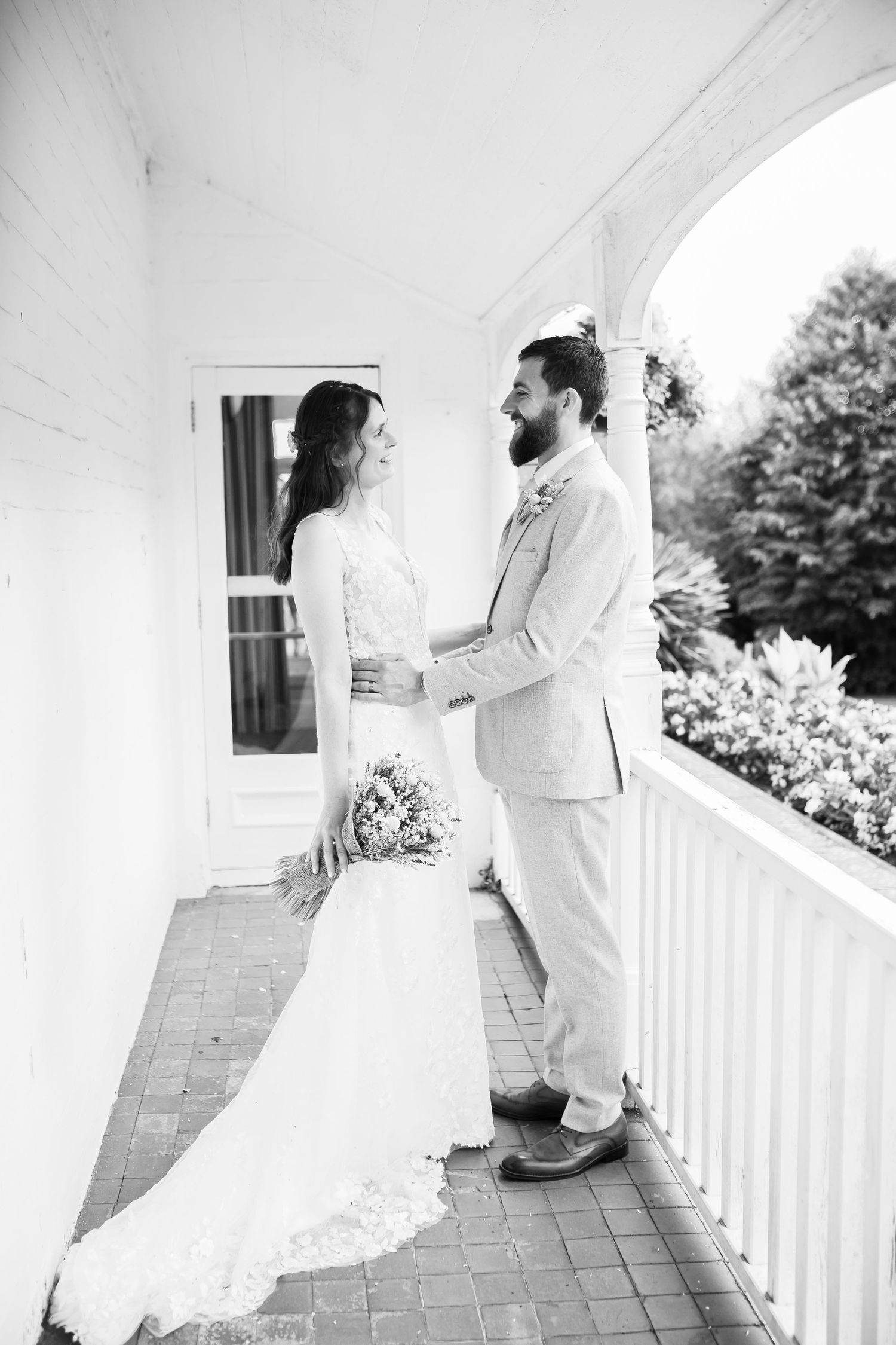 Newlyweds share an intimate moment on a white columned porch.