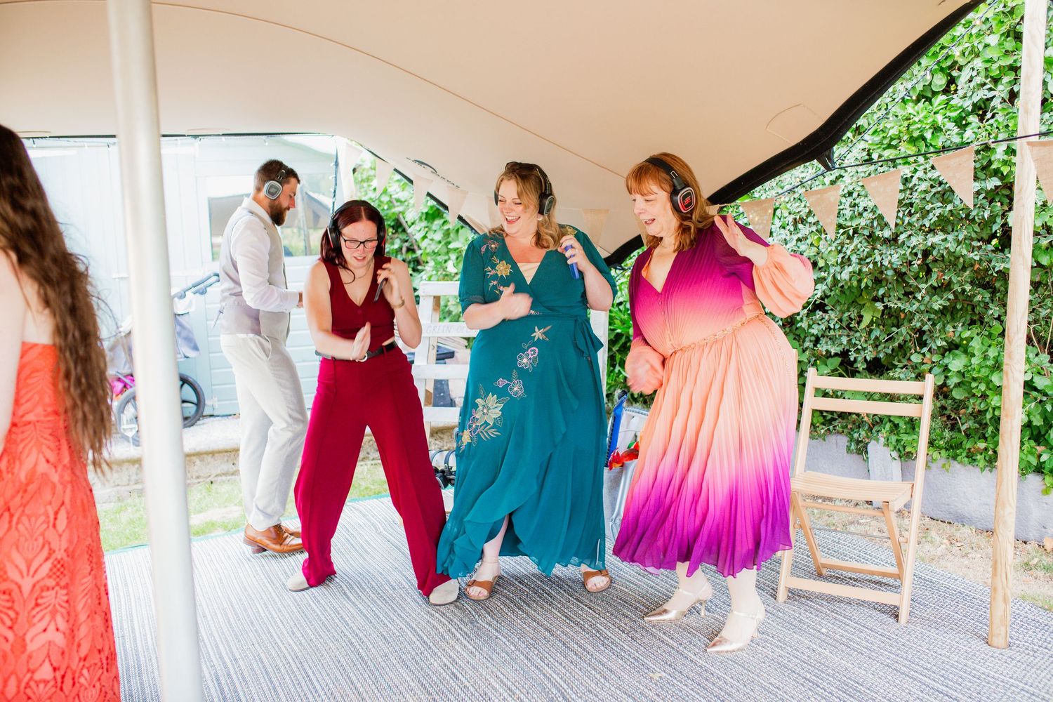 Wedding party in vibrant dresses celebrating under a white tent during reception.