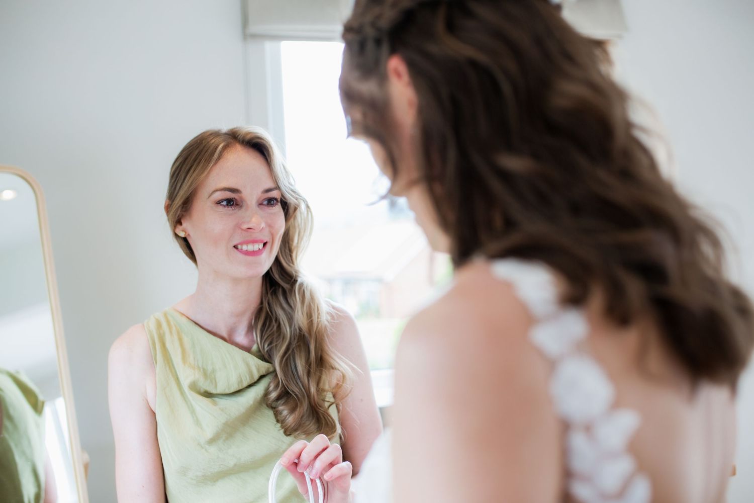 Two women in a bright room sharing a joyful moment before a wedding ceremony.
