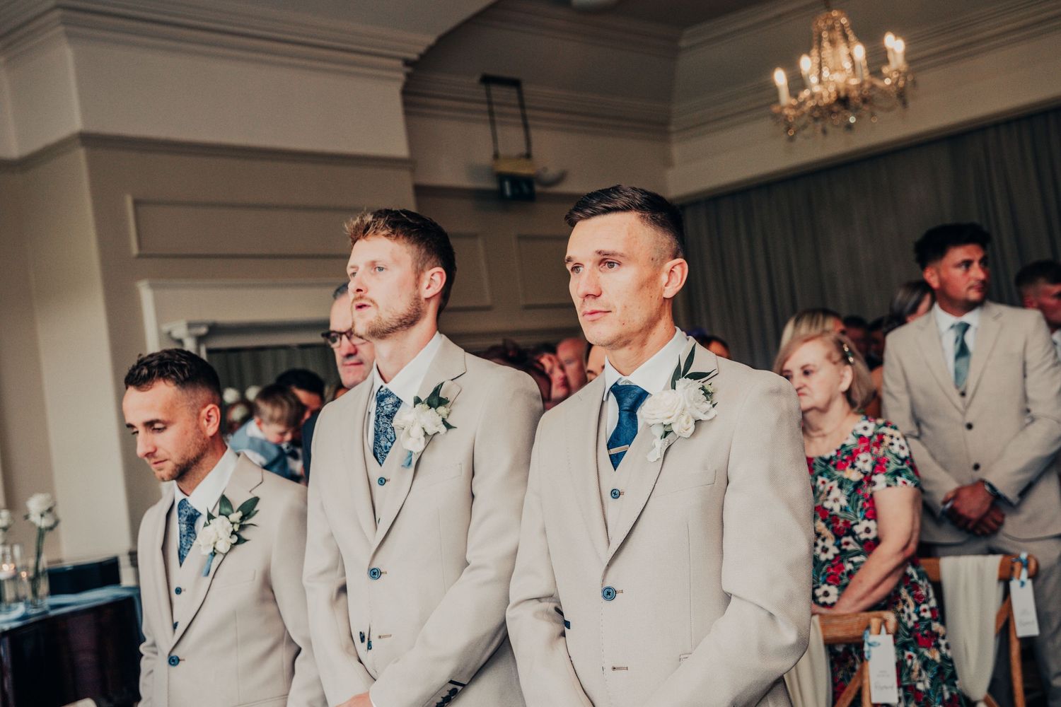 Groomsmen in light beige suits standing at attention during wedding ceremony.