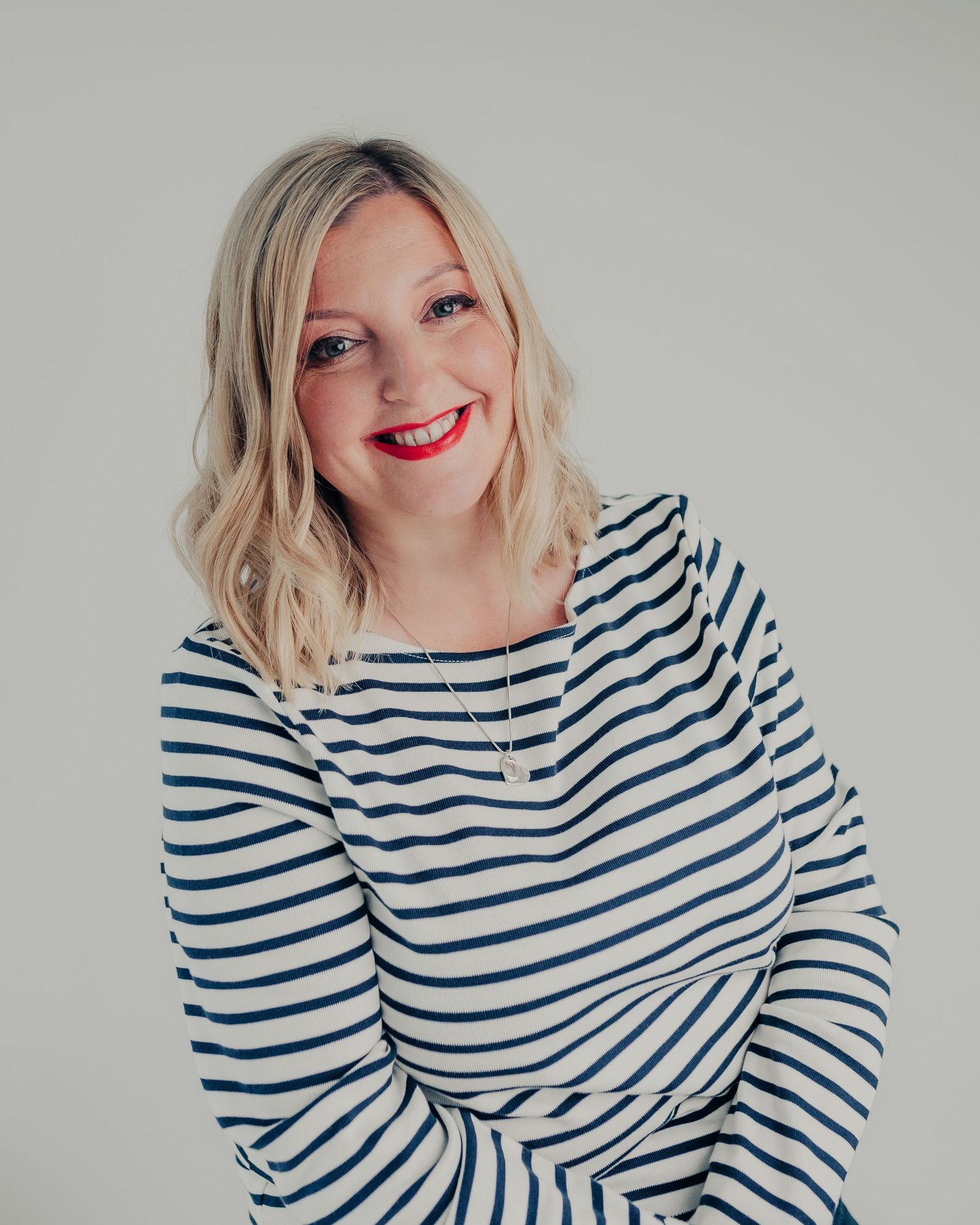 Portrait against grey background showing joyful expression wearing navy striped sweater.