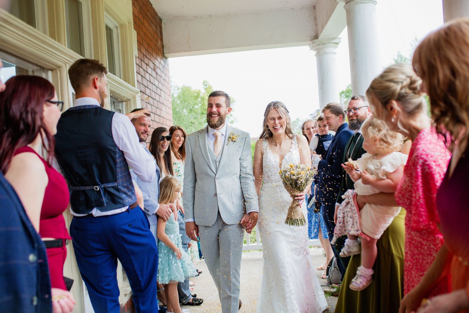 Wedding party celebration on a covered porch with guests in colourful summer attire.