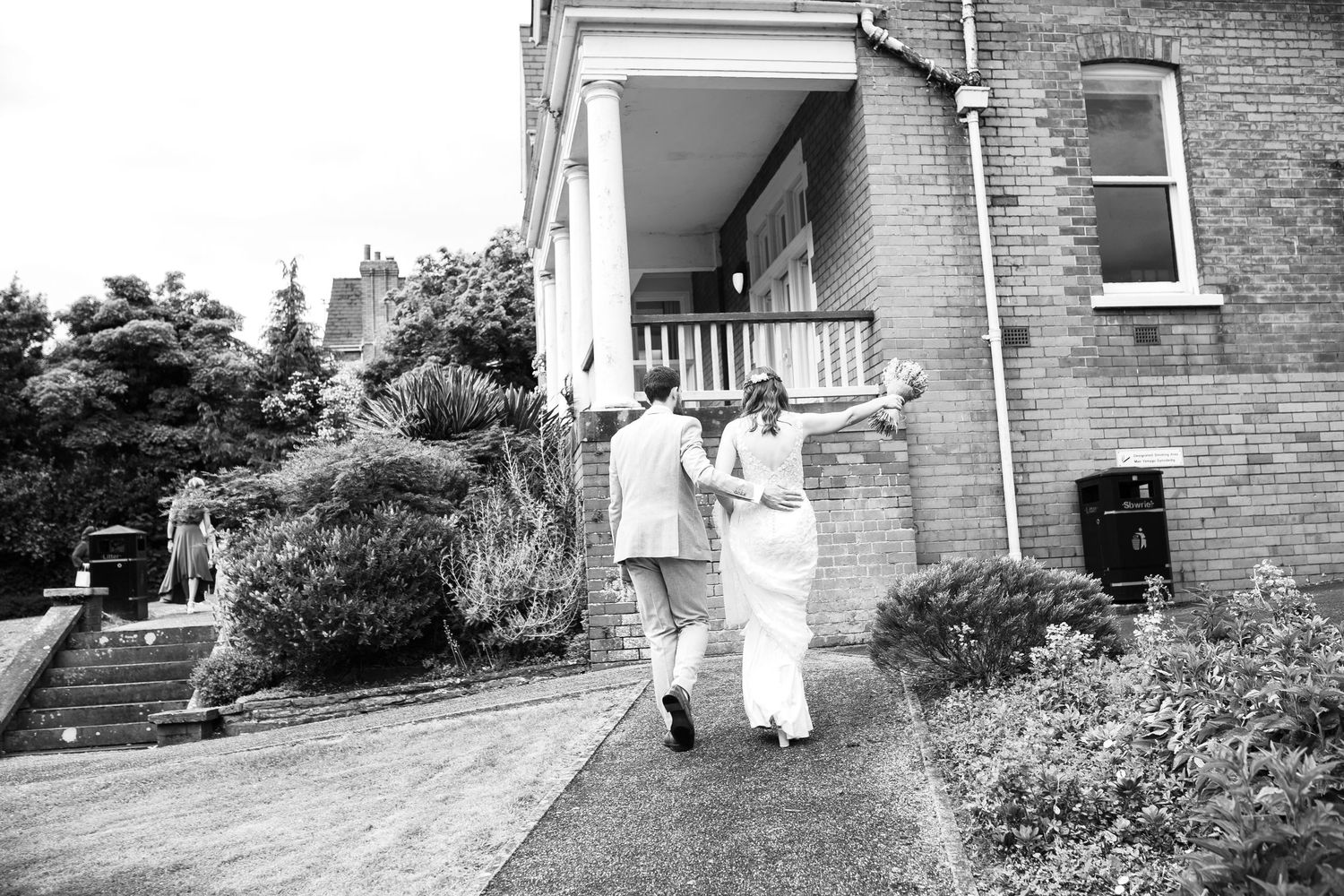 Black and white photo of a couple walking down a brick pathway at their wedding venue.
