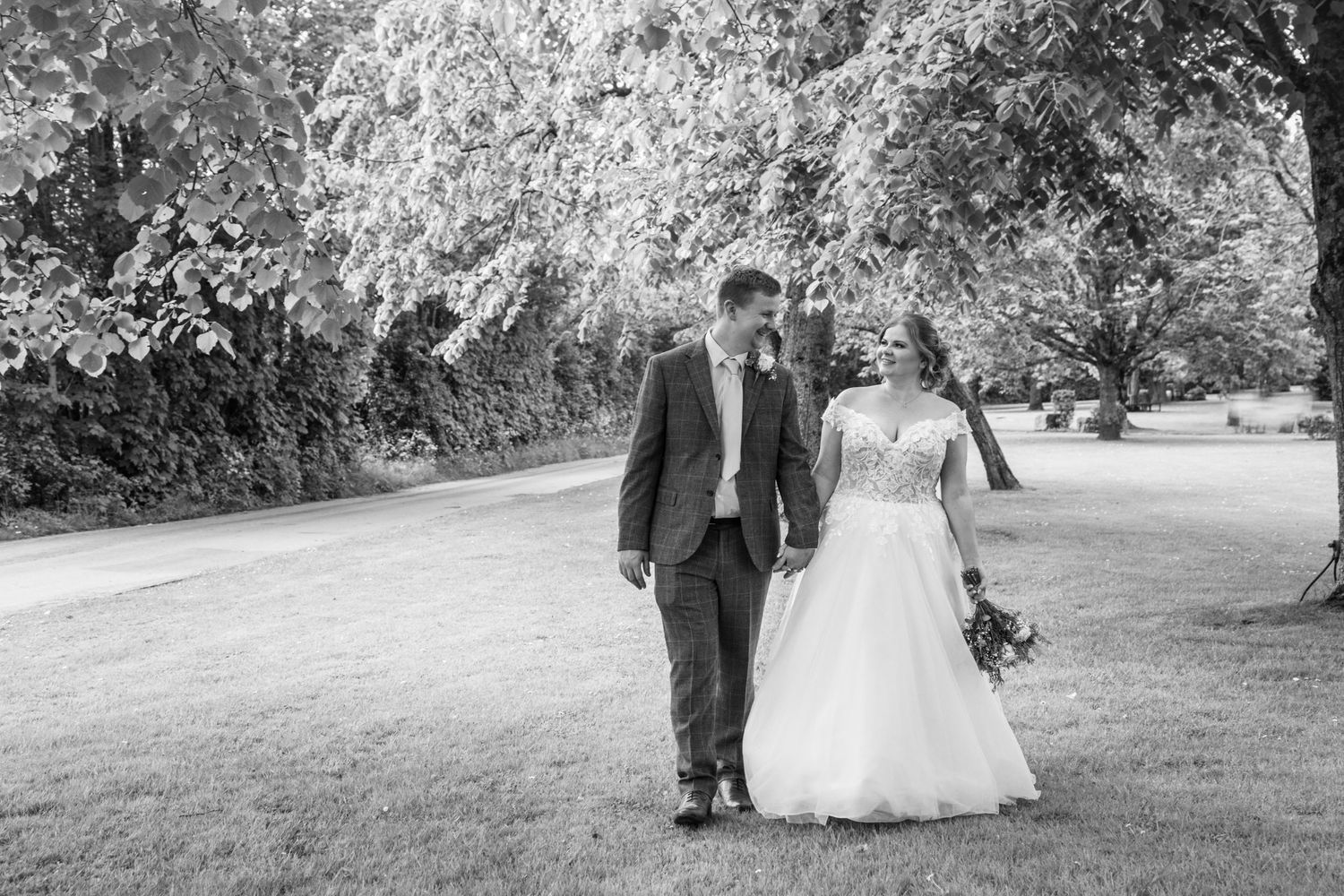 A black and white photo of newlyweds walking together on a serene garden path.