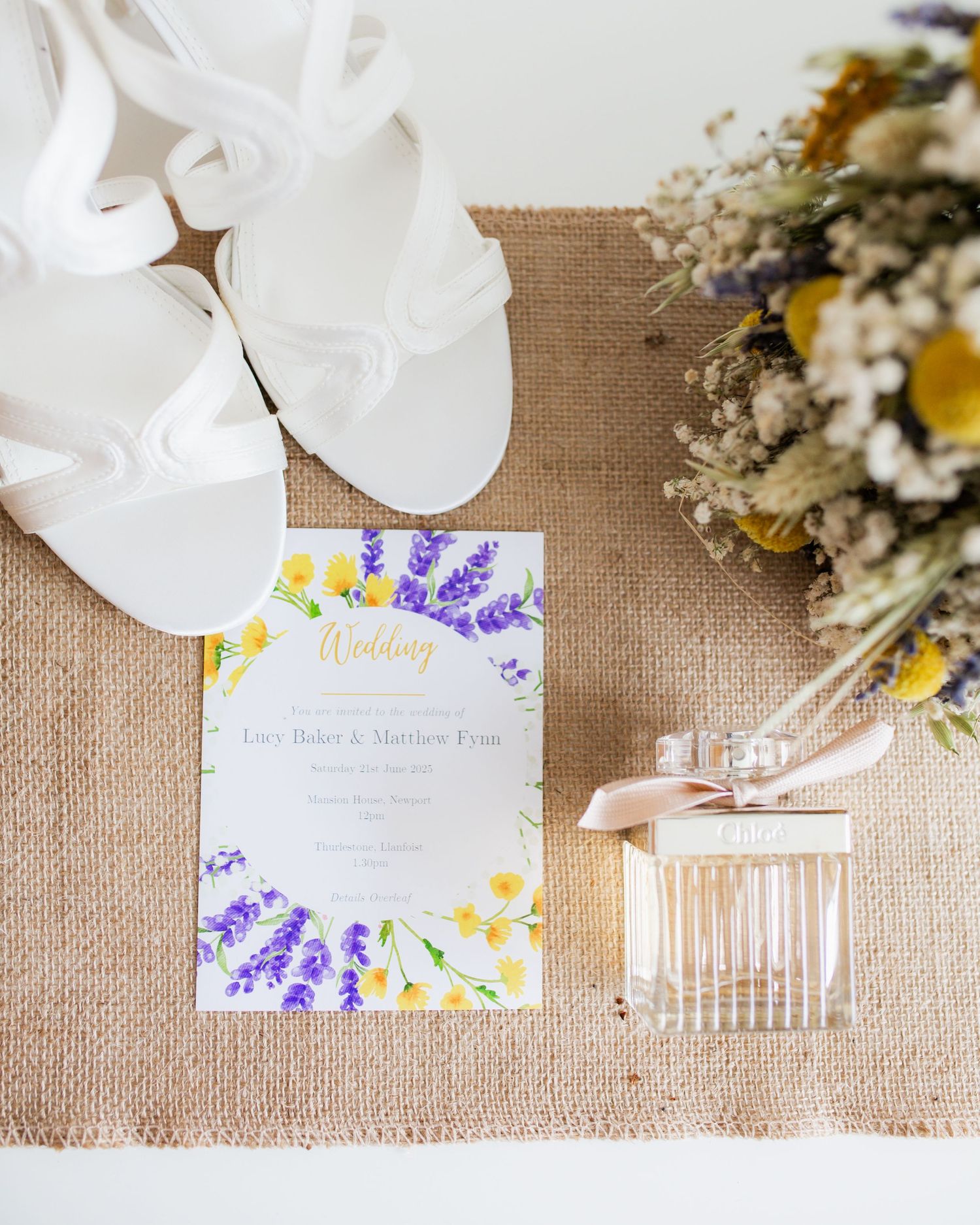 Wedding stationery with floral designs and lavender details arranged on burlap background.