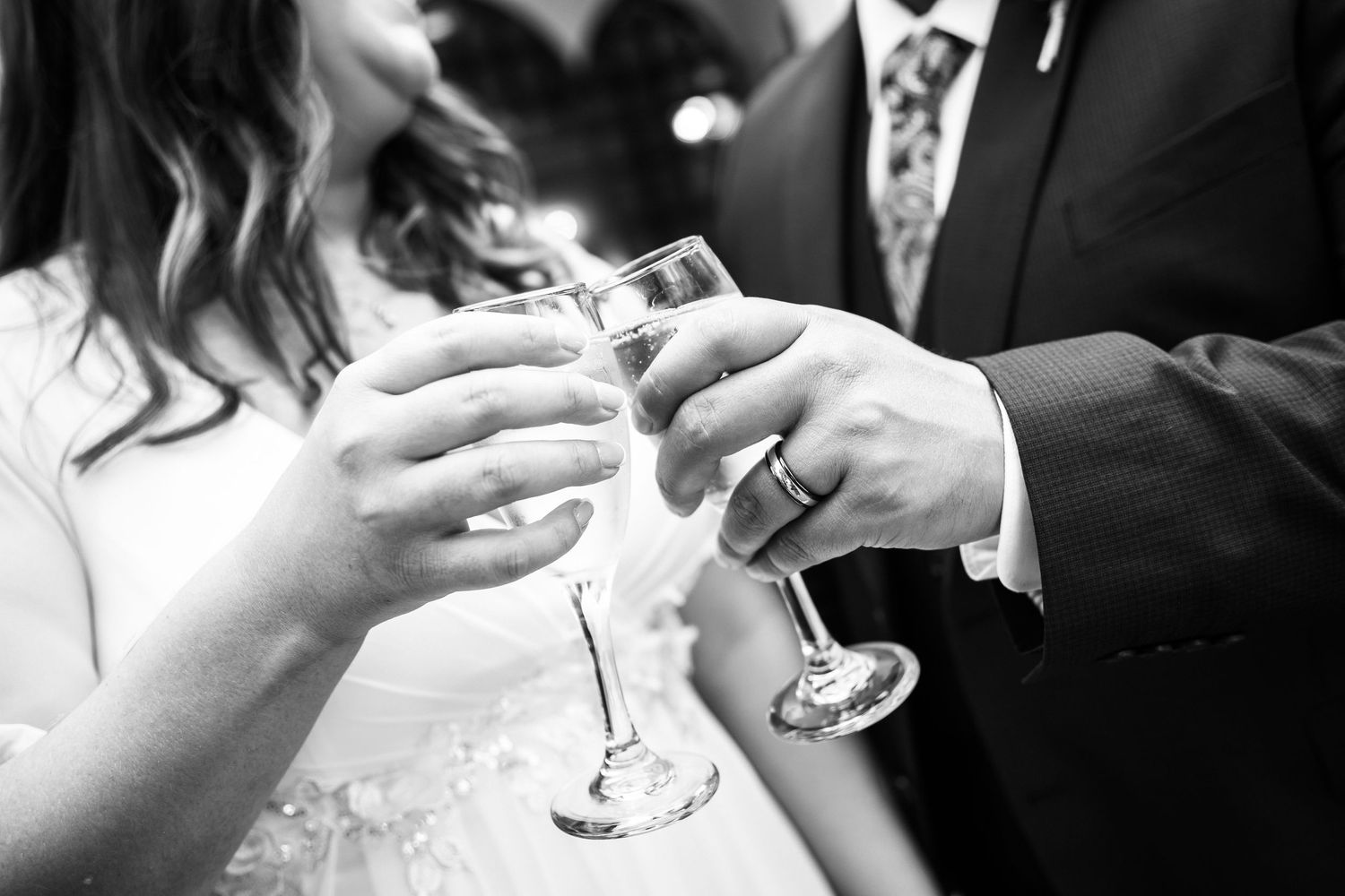 Close-up black and white shot of hands toasting with champagne glasses at wedding celebration.