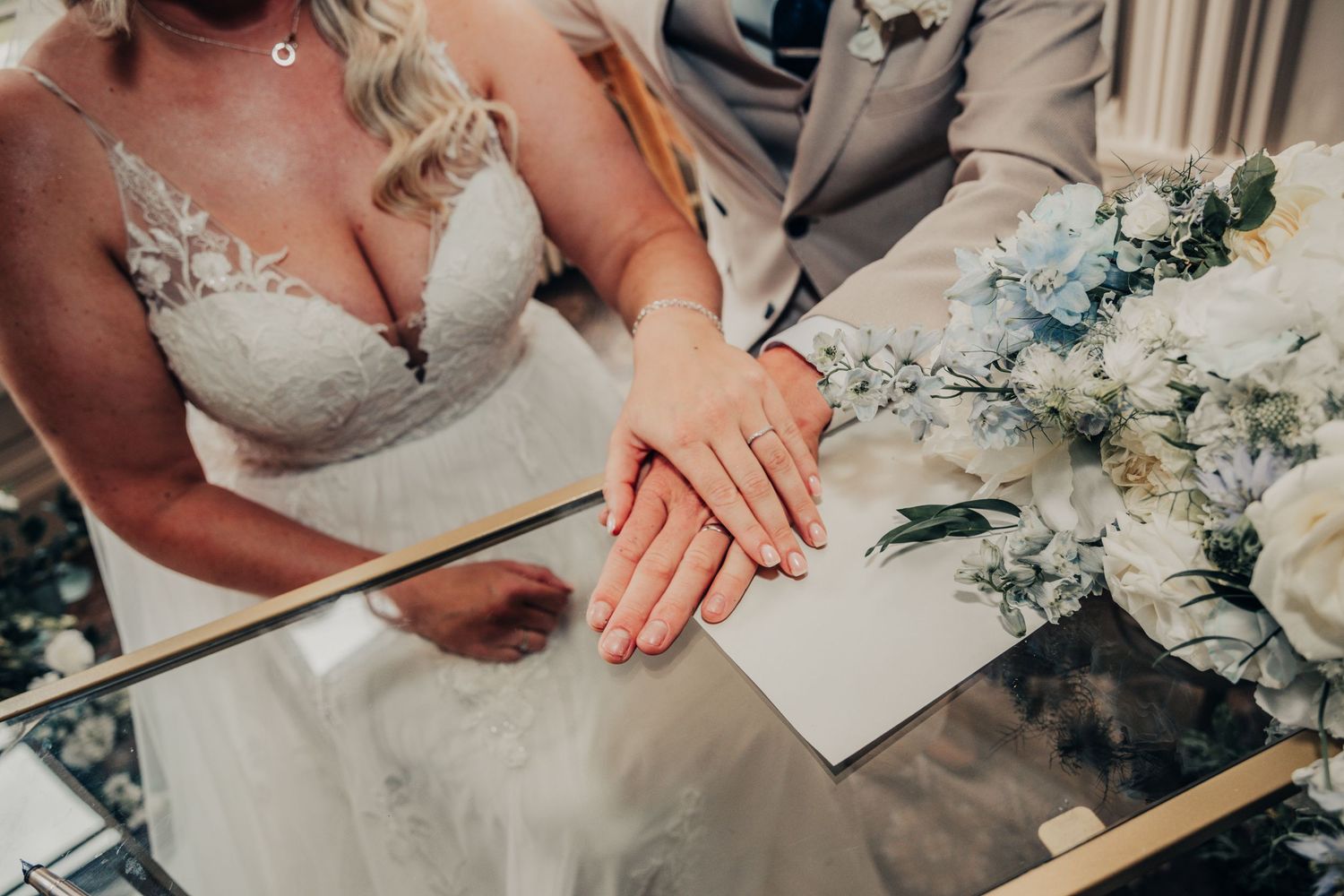 Close-up of wedding rings and white floral arrangements on a reflective surface.