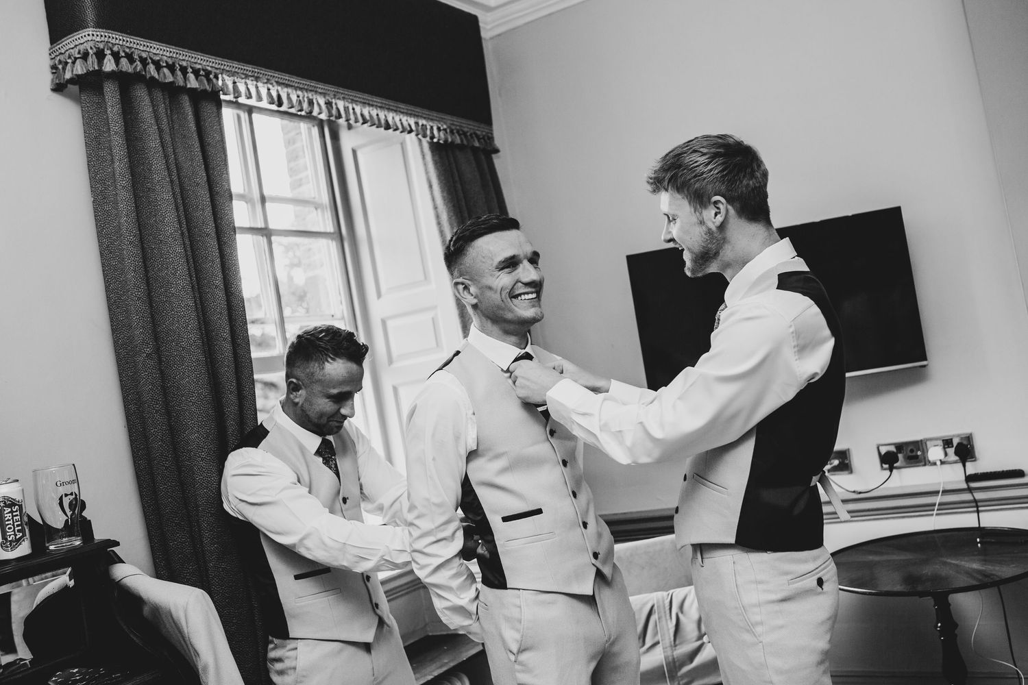 Groomsmen helping adjust formal attire during wedding preparations.